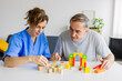 © Xavier Lorenzo - Female caregiver and senior man playing wooden shape puzzles game for dementia prevention