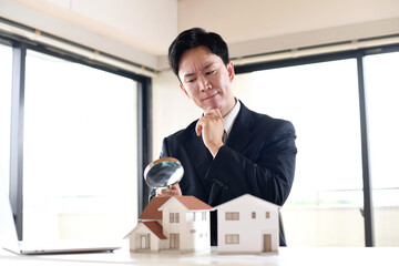 虫眼鏡で住宅模型を覗くスーツ姿の若い男性
