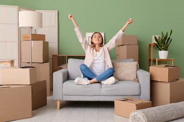 Wall Mural - Cheerful young woman sitting on sofa in new apartment. Moving house concept