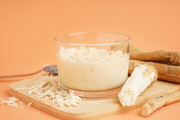 Wall Mural - Horseradish sauce in glass bowl with spoon and ground horseradish root on orange background