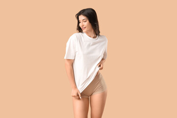 Wall Mural - Pretty young woman in t-shirt and panties on beige background