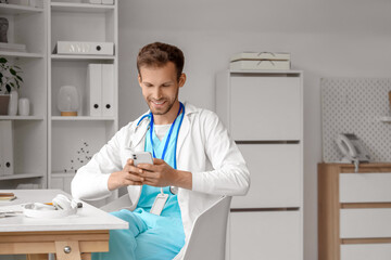 Sticker - Male medical intern using mobile phone at table in clinic