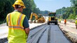 © Taqinaya - Civil engineer in yellow hard hat and high-visibility vest supervising road construction project