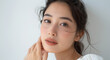 © Surachetsh - In a skincare commercial studio shoot, a beautiful Asian woman smiles gracefully with her hand resting on her cheek against a pristine white background, illuminated by studio lighting.
