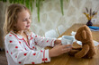© evgeniia_1010 - A pretty blonde girl in beautiful pajamas with hearts is having a delicious breakfast and feeding her beloved ivy bear. The idea of proper and balanced nutrition and games for children.