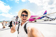 © Davide Angelini - Happy tourist boarding on a plane at the airport - Handsome young man taking selfie in front of airplane - Summertime holidays and transportation life style concept