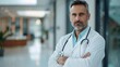 © horizon - Handsome middle-aged doctor in a white coat holding a stethoscope, a portrait of a confident male health care professional standing in a hospital entrance hall.
