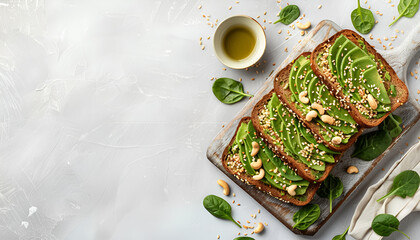 Wall Mural - Avocado sandwich or toast on rye bread with spinach, crushed cashew nuts and sesame seeds, on wooden board, on white table, top view, space for text