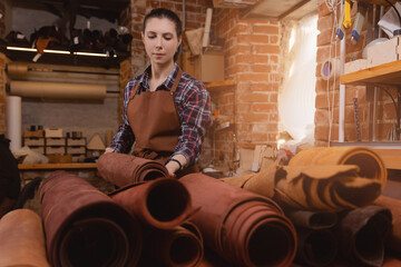 Wall Mural - Portrait of happy young woman craftsman tailor with brown rolls of natural color leather on atelier workshop. Concept small business DIY handmade