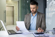© Liubomir - A dedicated businessman reviews important financial documents while working in a modern office environment.