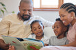 © Mdlungu/peopleimages.com - Reading, African family and book in living room on weekend to relax, storytelling and parents on couch. Black man, woman and kids on sofa for care, fantasy and trust or bond together with love