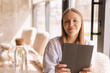 © zvkate - Attractive happy smiling blonde woman wear shirt sitting with tablet computer in cafe. Beauty girl student using tablet computer for social media, studying or reading news.