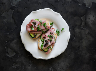 Wall Mural - Delicious breakfast, snack, tapas, appetizers - sandwiches with ham, cucumber and microgreens on a dark background, top view