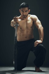 Poster - Portrait, kneeling and Asian man with sword in studio for wellness, exercise and fitness or martial arts. Warrior, training and blade for ninja by black background for karate for dojo in Japan