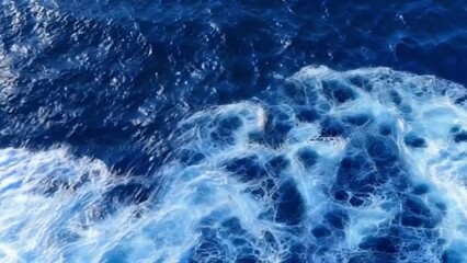 Wall Mural - aerial perspective, the deep navy blue expanse of the ocean stretches out beneath, with white waves crashing and splashing against its surface.