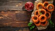 © Otseira - Homemade Crispy Deep-Fried Onion Rings with Ketchup on a rustic wooden board, top view. flat lay. Space for text.