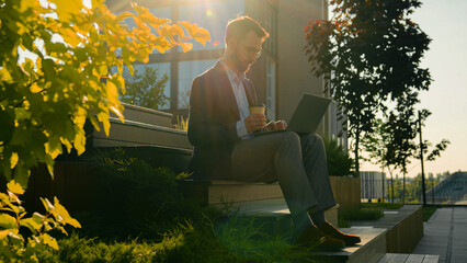 Caucasian business man freelancer work with laptop computer male businessman office worker on steps modern university campus in sunny city browsing website chatting outdoors drinking coffee takeaway