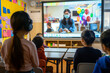 © Tatiana - Children Attending Virtual Class with Teacher on Screen in Classroom