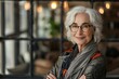 © Vera - powerful portrait of a confident and proud elderly female entrepreneur in her office, wearing CEO glasses and crossing her arms with a smile of satisfaction for her successful career