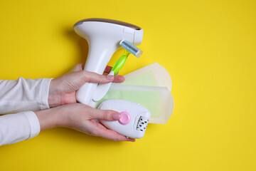 Wall Mural - A modern epilator for removing unwanted body hair at home, wax strips, a mechanical epilator and a razor on a colored background in female hands