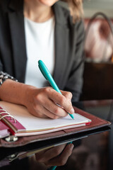 Close-up of a female hand writing on an blank notebook with a pen. Leather notebook on a black glass table