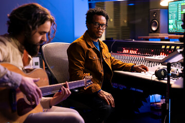 Aufkleber - Singer recording electro acoustic guitar in professional music studio, playing musical instrument to compose a new hit song with his producer. Diverse musicians singing a record in control room.