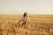 © arthurhidden - A happy young woman in casual attire enjoying a walk in a beautiful golden wheat field at sunset.