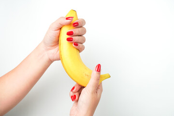 Hands of a woman with bright red nail polish holding large curvy banana fruit isolated on white background. Illustration for sex workers, sexual scenes, and male genitalia penis.