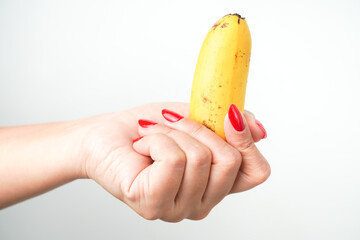 Canvas Print - Hands of a woman with bright red nail polish holding small sized banana fruit isolated on white background. Illustration for sex workers, sexual scenes, and male genitalia penis.