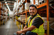 © Kien - Smiling warehouse worker in a yellow vest with a hand truck working at a desk and holding a box
