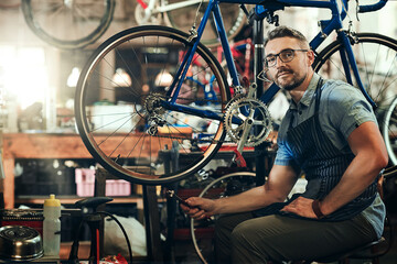 Wall Mural - Man, portrait and fixing at work in bicycle repair shop or maintenance garage. Bike, mechanic and service with a professional handyman for startup, small business and mechanical vehicle workshop