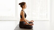 © Prostock-studio - A woman is sitting cross-legged on the floor, practicing yoga. She is focused and holding a pose with her eyes closed, showing concentration and mindfulness, copy space