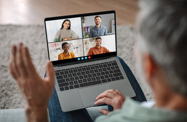 Poster - Senior man sits on a couch, his back to the camera, actively participating in a video conference call on his laptop. Screen displays four participants, all smiling and engaging in the virtual meeting