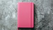 © AkuAku - A closed pink notebook set against a gray backdrop