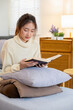 © MIND AND I - Young woman sitting and reading a book from the couch.