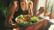 © VK Studio - A person in athletic wear enjoys a fresh, colorful salad in a well-lit room, signifying healthy eating and a fitness lifestyle.