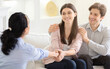 © Prostock-studio - A young couple smiles warmly while having a conversation with a counselor in a cozy, sunlit living room. The counselor is attentively listening and engaging with the couple, shaking hands
