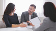 © Prostock-studio - Couple sits at a table in an office, looking at documents with a financial advisor. Advisor holds up a sheet of paper while the couple looks attentive, suggesting they are in the midst of discussion
