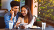 © Prostock-studio - A young African American couple is seated in a cozy cafe during the afternoon, sharing earbuds and smiling as they watch something on a smartphone. They seem relaxed, enjoying each others company.