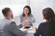 © Prostock-studio - A woman in a gray blazer smiles and shakes hands with a man sitting across from her at a table. A third person sits to the woman right and observes the interaction.