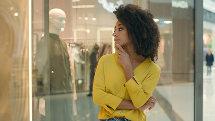 African American woman looking at showcase mannequin shopping mall thinking decision pondering choose female girl new collection boutique fashion style buyer clothes customer exclusive store selection