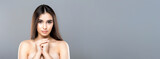A woman with no clothes, her hands crossed over her chest, standing in a simple pose. The focus is on her body and the gesture of covering herself, panorama with copy space