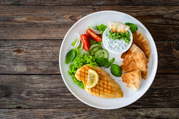 Poster - Seared chicken breast, pita bread and tzatziki on wooden table