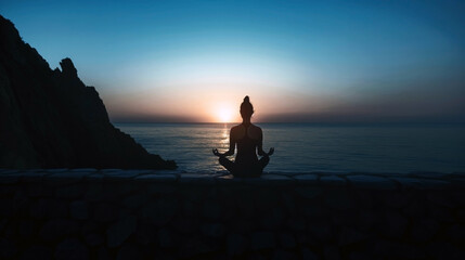 Poster - Silhouette of a person meditating in a lotus position on a stone wall by the sea during a serene sunset.