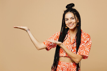 Wall Mural - Young smiling fun happy Latin woman she wears orange casual clothes point hands arms aside indicate on area mockup isolated on plain pastel light beige background studio portrait. Lifestyle concept.