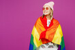 © ViDi Studio - Young fun happy lesbian woman wear pink clothes wrapped in striped rainbow flag look aside on area mockup isolated on plain purple background studio portrait. Pride day June month love LGBTQ concept.