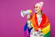 © ViDi Studio - Young happy lesbian woman wrapped in rainbow flag wears pink clothes listen music in headphones scream in megaphone isolated on plain purple background studio. Pride day June month love LGBTQ concept.