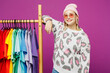 © ViDi Studio - Young smiling happy lesbian woman wear pink animal clothes show colorful t-shirt wardrobe on rack at store isolated on plain purple background studio portrait. Pride day June month love LGBTQ concept.