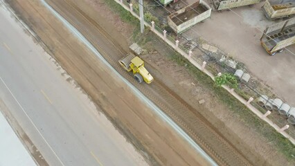 Wall Mural - Aerial view of construction tractor car, bulldozer, or backhoe digging road or street in traffic transportation and agriculture concept. Engine working in urban city town.