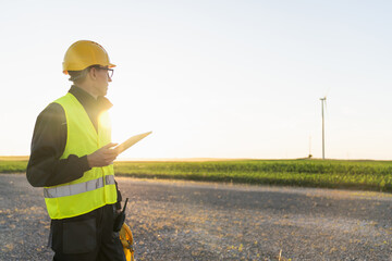 Engineer with digital tablet works on a field of wind turbines